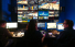 Video: Three people sit at a bank of monitors in a dark room