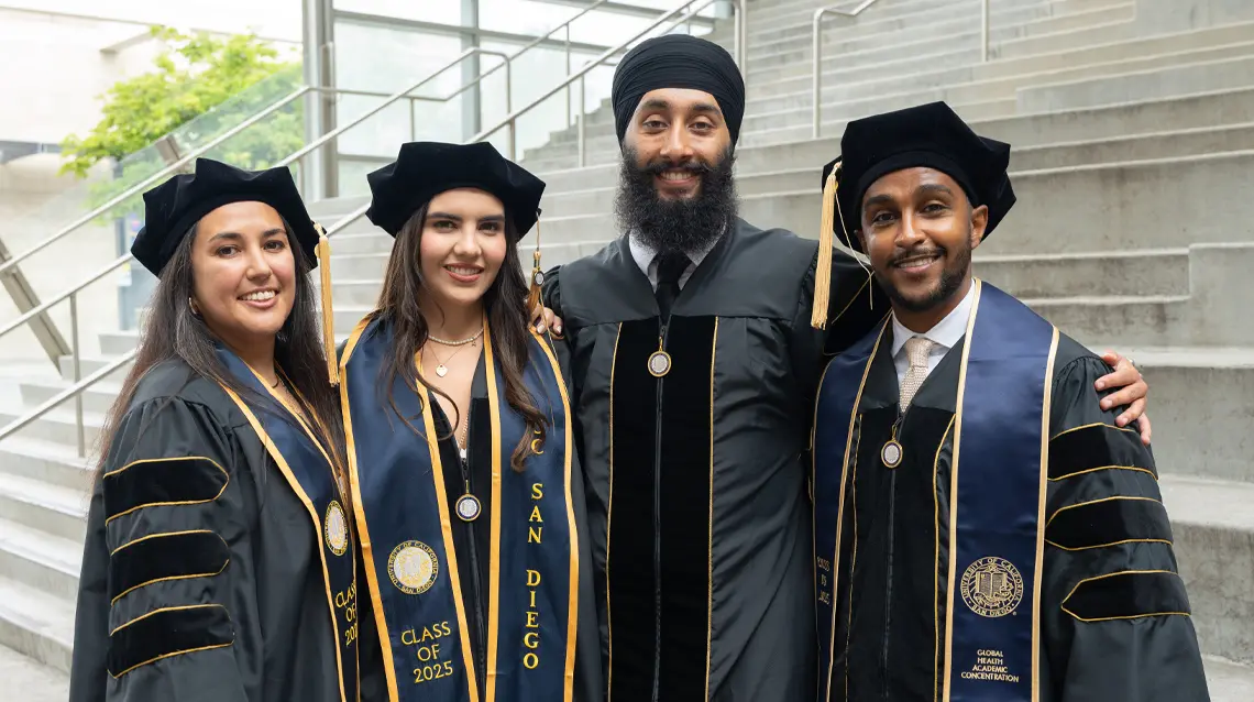 two male and two female medical school graduates standing with arms around one another smiling at the camera