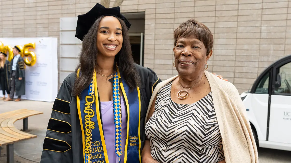 black female graduate standing with arm around older female family member both smiling at the camera