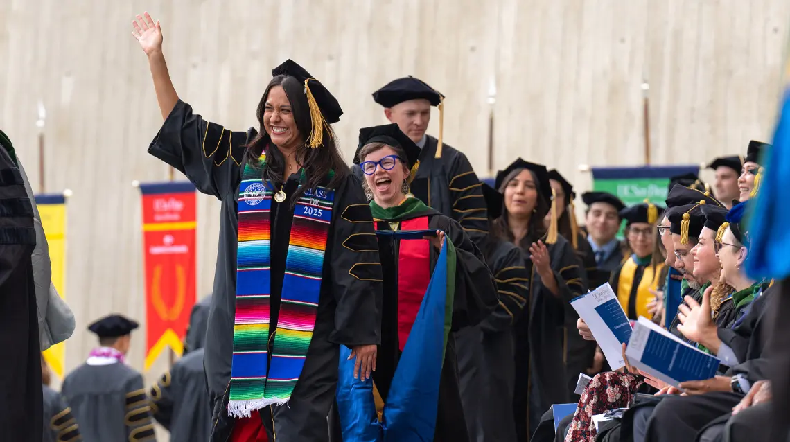 Image of Camilla Reyes Martinez waving towards the crowd as she walks across the stage at commencement
