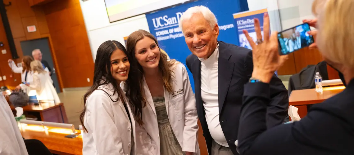 Former UC San Diego Chancellor and UC President Emeritus Richard C. Atkinson posing for photos with two female students in white coats