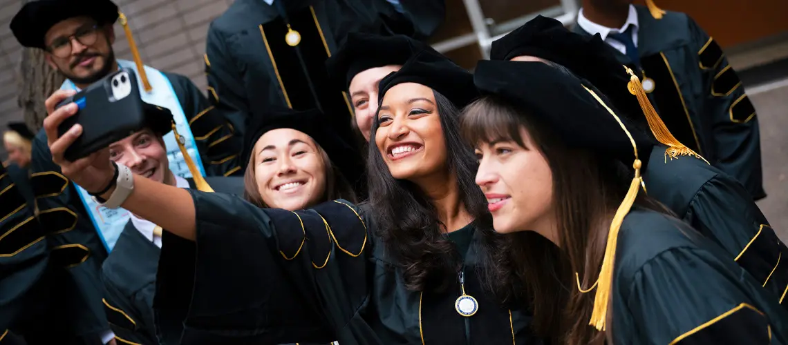 Four female graduates taking a selfie in their commencement regalia