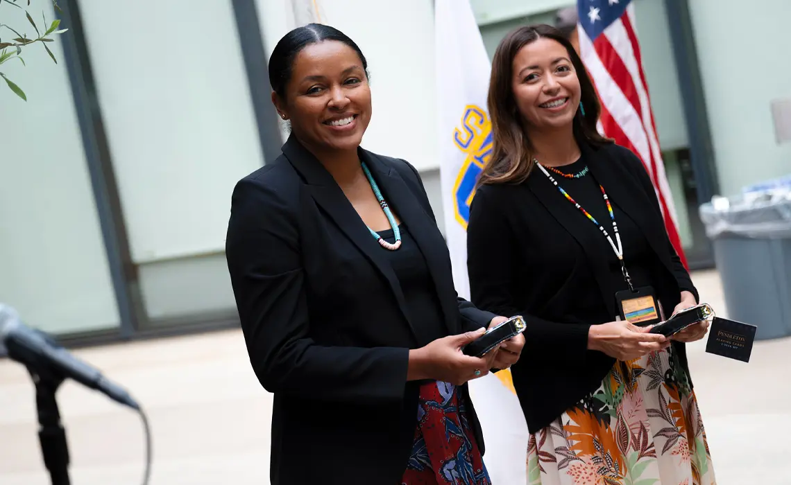 Two female faculty members smiling at the camera holding small box gifts in their hands
