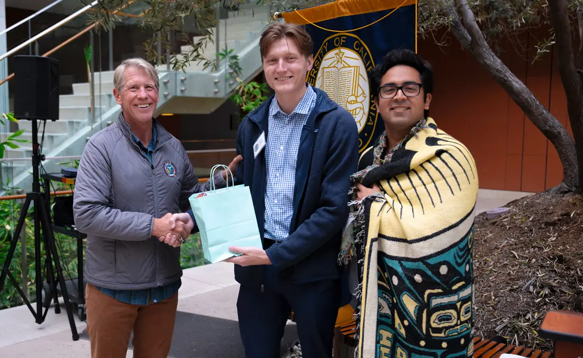 Two male students handing a gift bag to a male faculty member