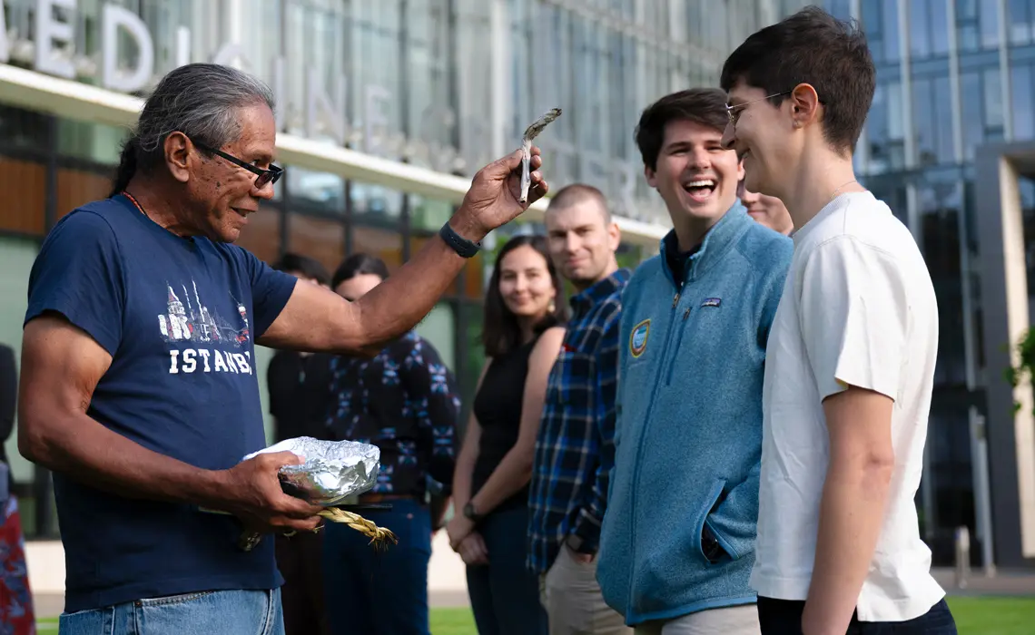 Stanley Rodriguez, Ed.D performing a smudging ceremony with two male students who are both smiling and laughing