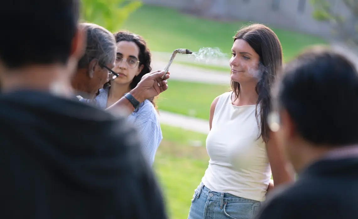 Stanley Rodriguez, Ed.D giving a blessing to a female student, smoke is seen floating over her face