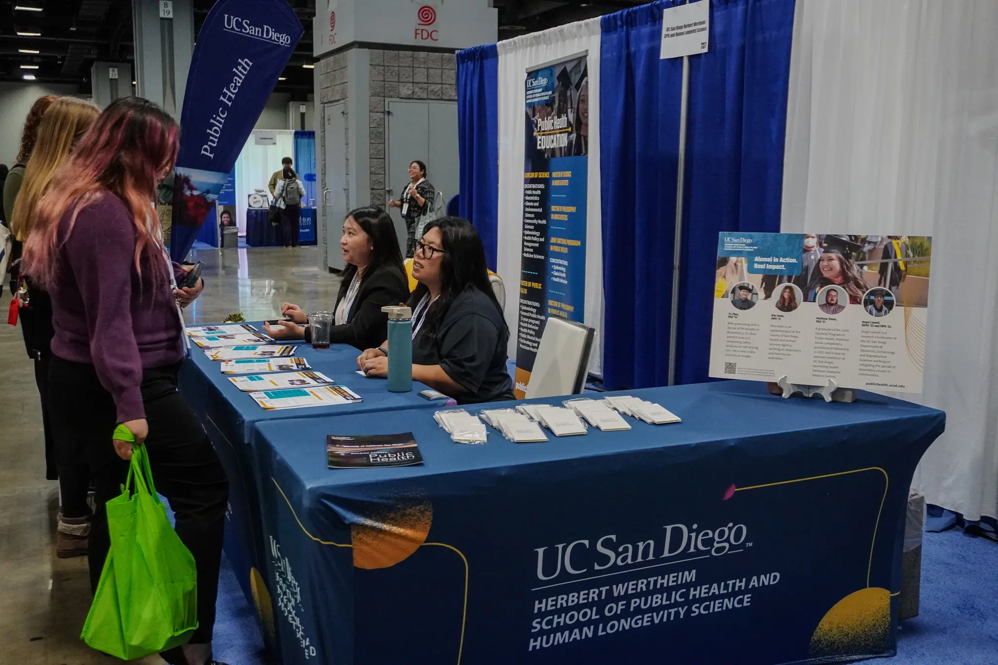 Two people sitting at a table talking to interested people at expo booth