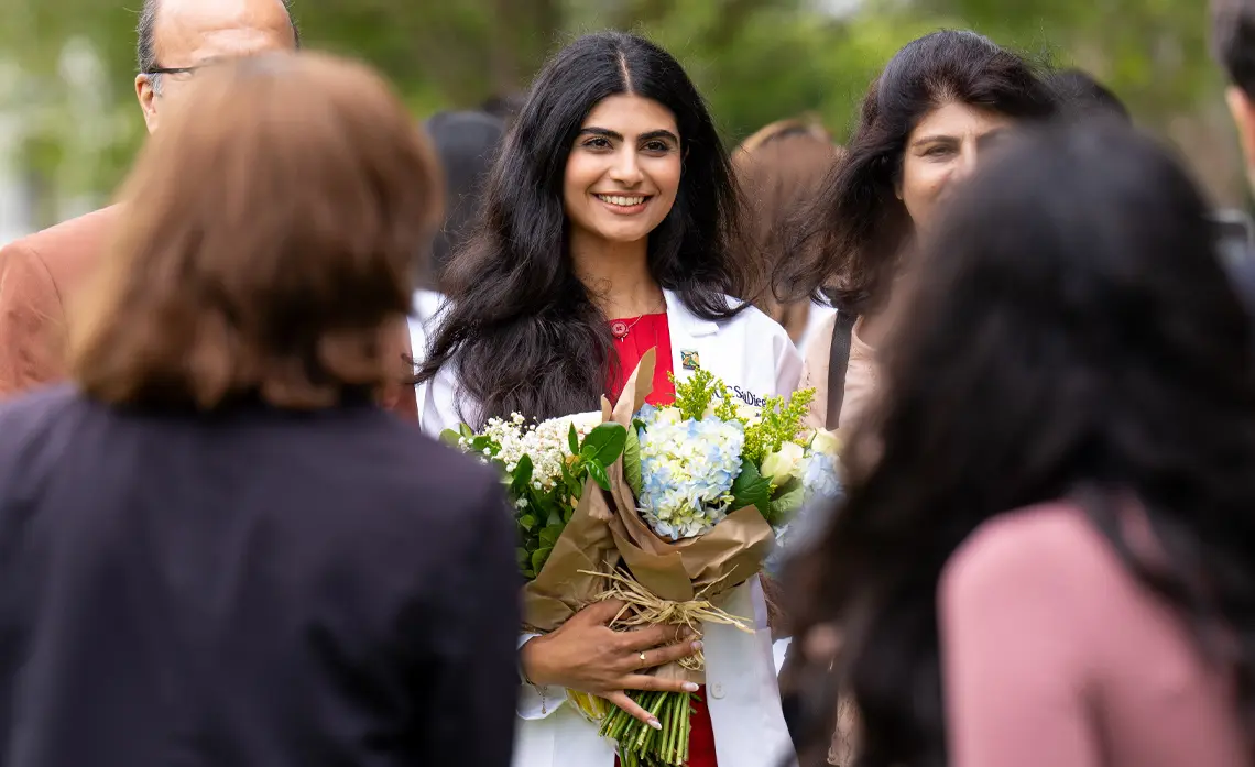 female student smiling and holding bouquets of flowers, in center of family members