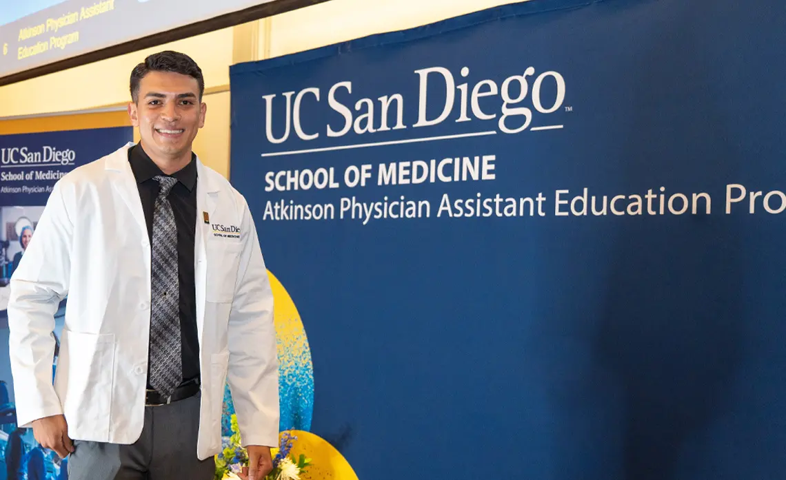 male student wearing white coat walking across the stage at White Coat Ceremony