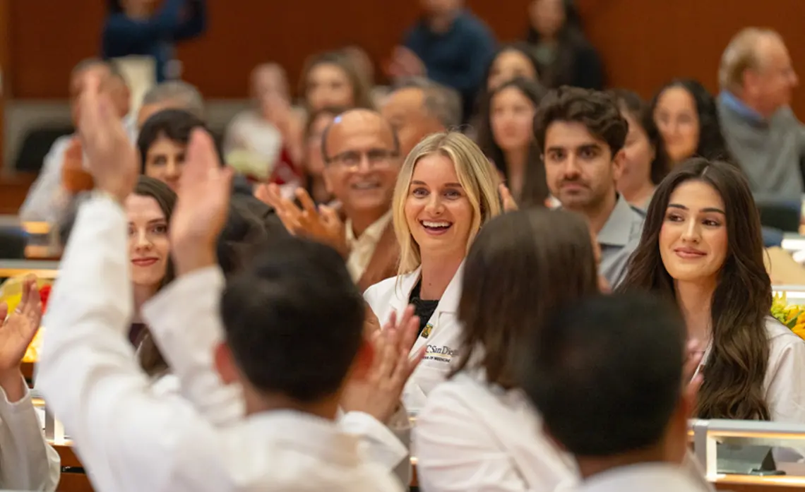 Group of PA students in the Ong Family Auditorium, blurred around edges focused on two female students in the center.