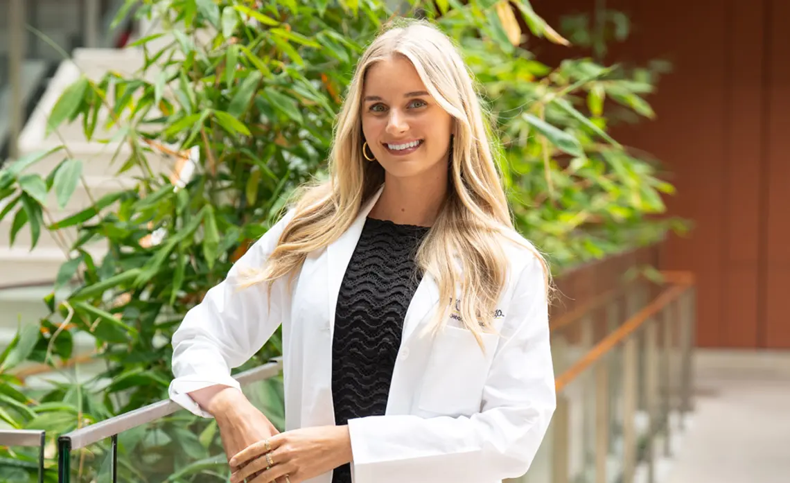 Blond female posing outside in front of a tree and smiling at the camera
