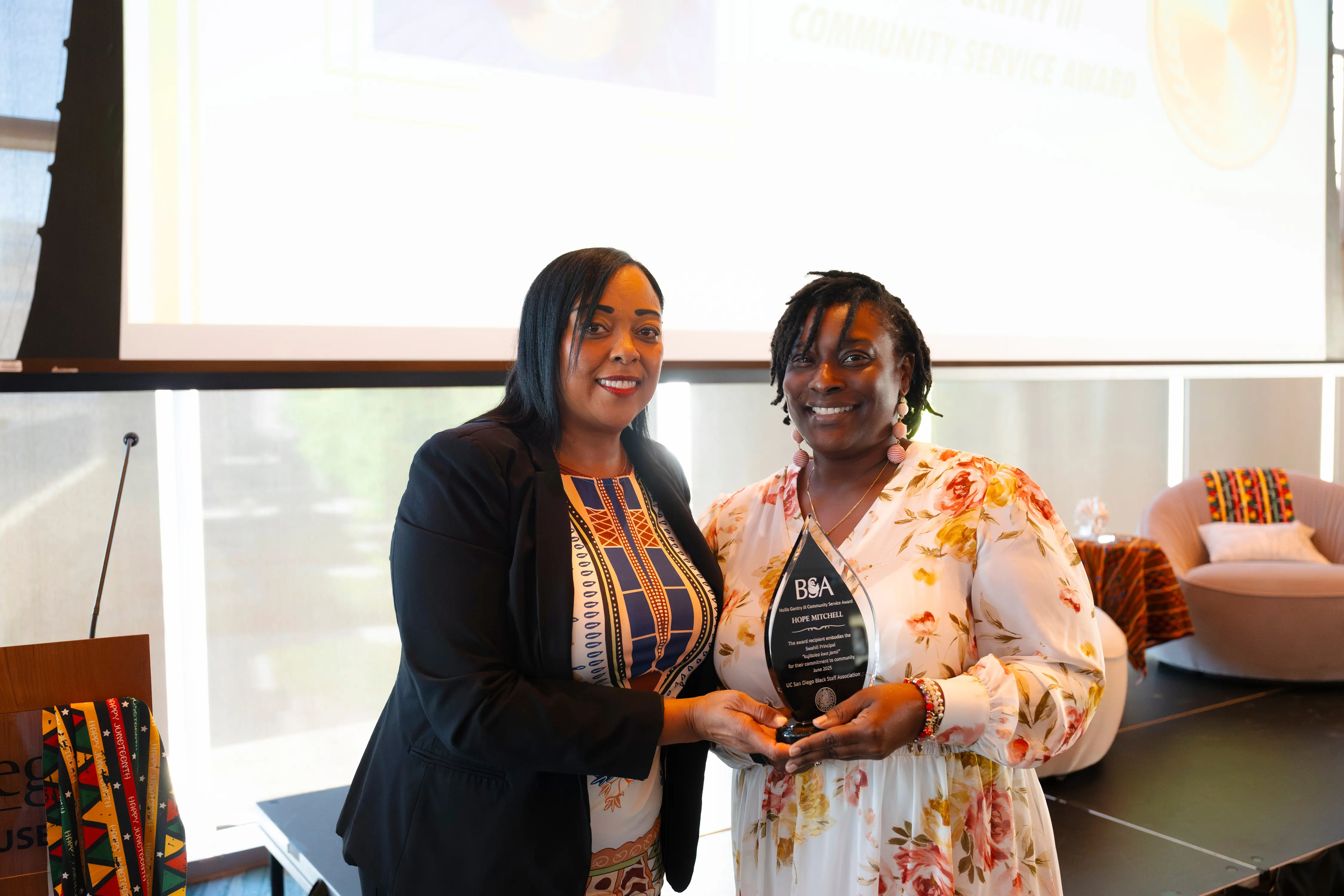 Two people smile at the camera with one holding an award