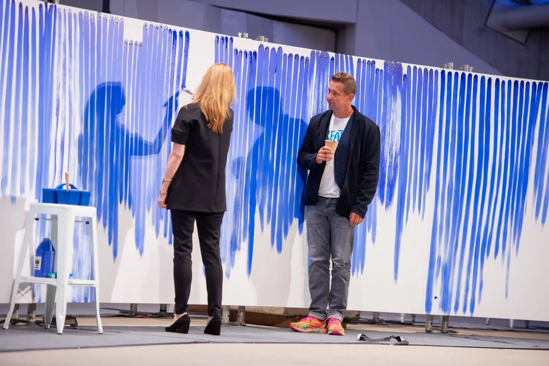 A person - Laura Linney - paints a blue line on a canvas.