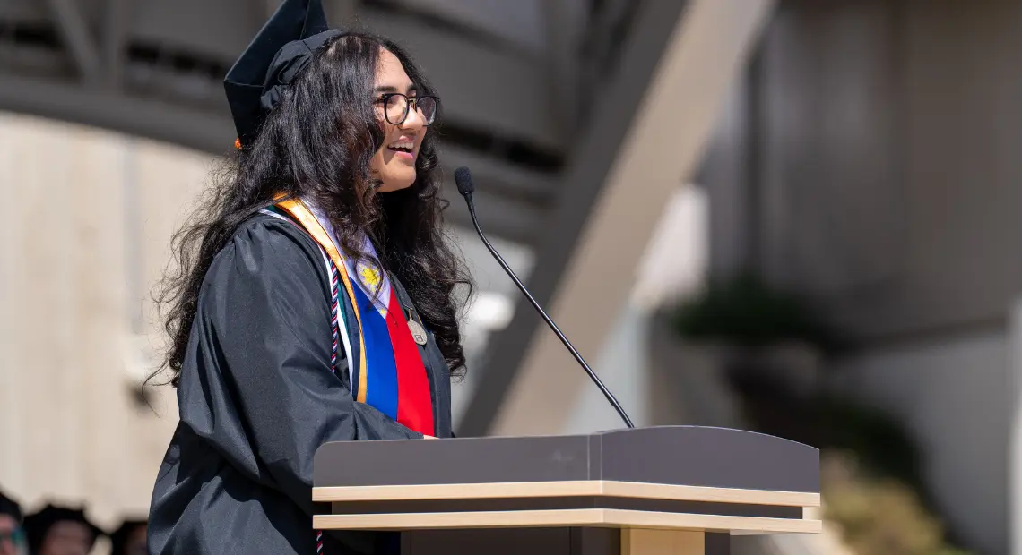 Lindsey Jules Ruiz-Estacio standing at the podium during the Herbert Wertheim School of Public Health and Human Longevity Science 2025 Commencement.