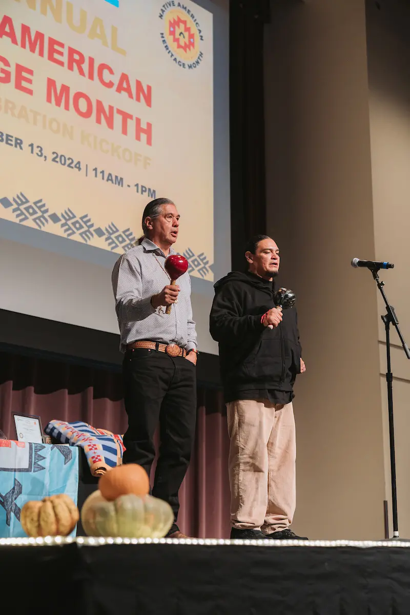 Two men hold traditional shakers while singing.