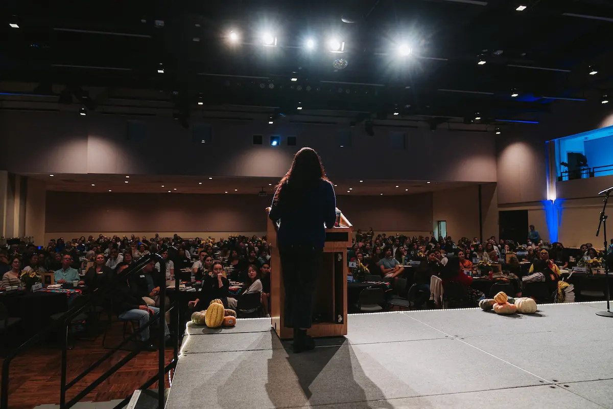 View from behind of a woman standing at a podium looking at a large crowd.