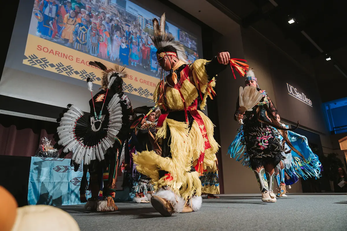 A group of people in traditional attire dance on stage.