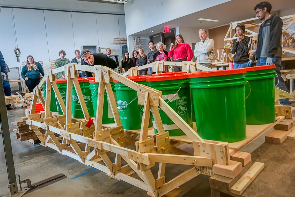 Picture of a wooden bridge loaded with buckets of sand, with a professor looking at it.
