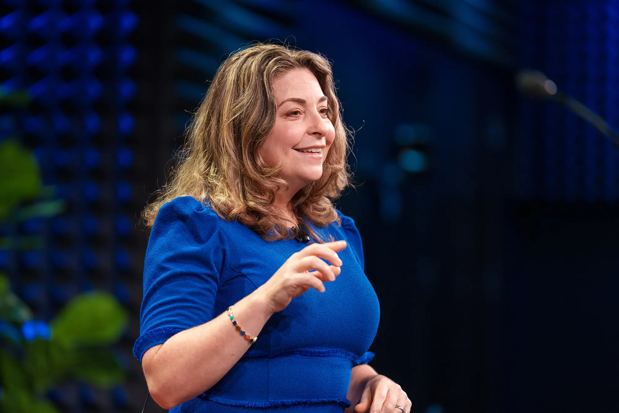 Woman in blue speaks to an audience as a keynote speaker, using expressive hand gestures.