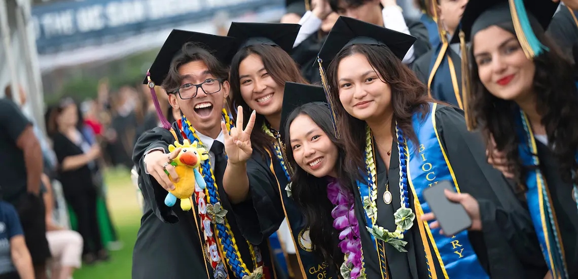 Five graduates, one holding a Fluffy Sun God, pose for photo
