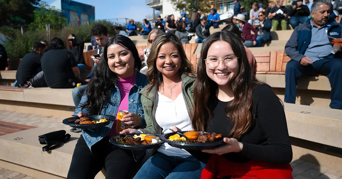 Three women smile while holding plates of food