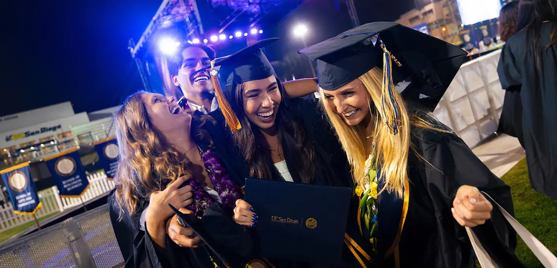 Four graduates hug and smile