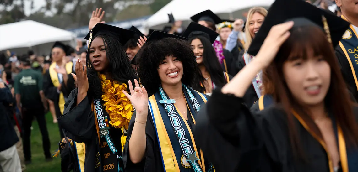 One graduate does a trident sign and smiles while another blows a kiss