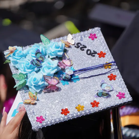 Photo of a silver graduation cap that has blue roses, butterflies and the numbers