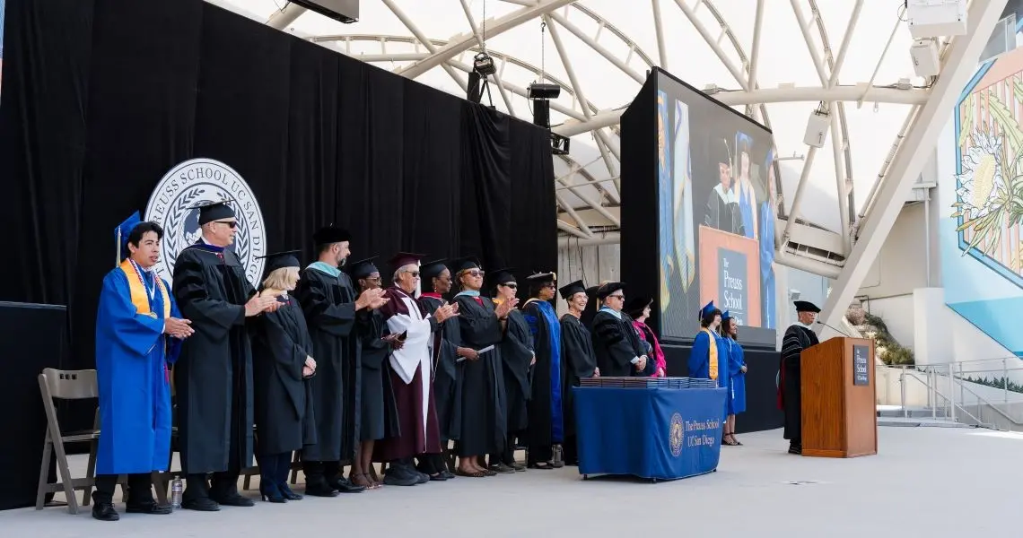 University and school leaders in commencement attire standing and applauding