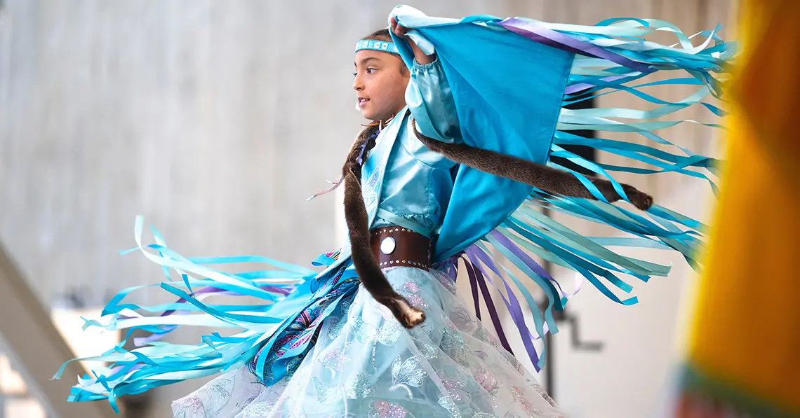 Child with Soaring Eagles Powwow Dance Group of San Diego dances in traditional blue outfit