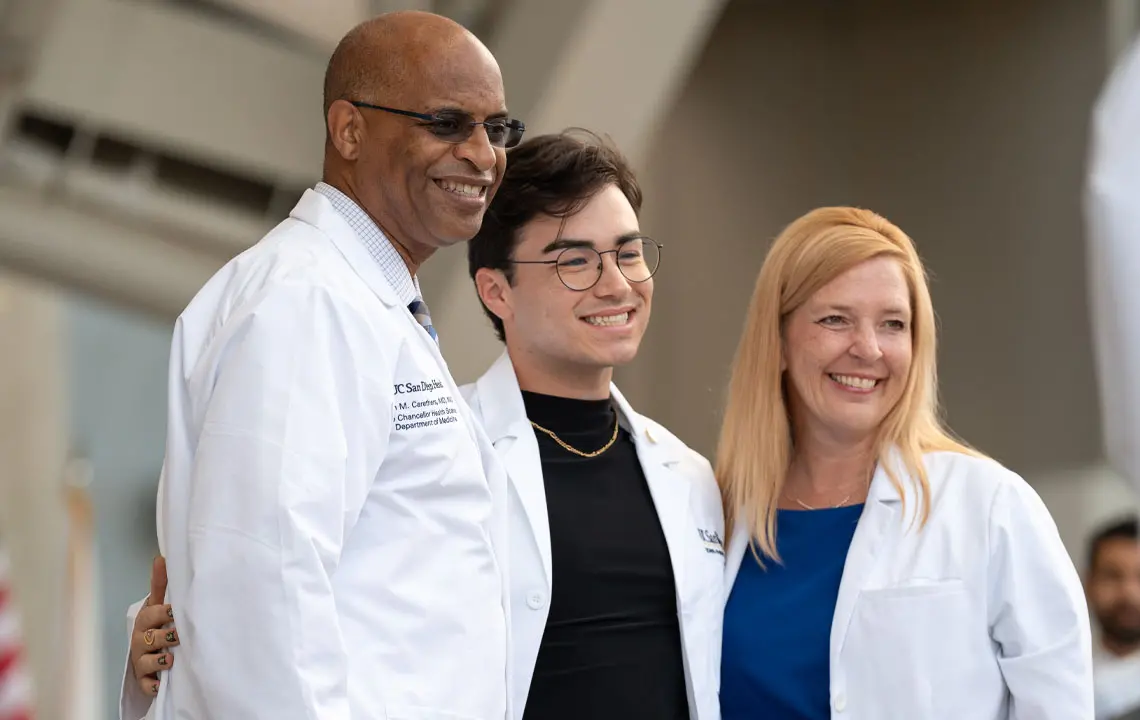 Medical student wearing white coat posing with faculty members