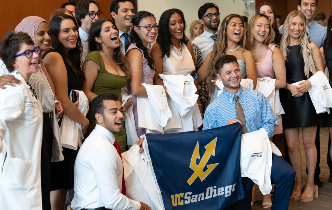 Red academic community members groups together smiling holding UC San Diego flag