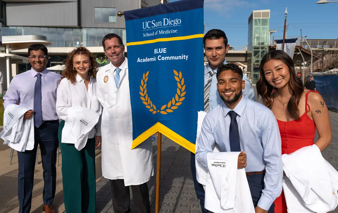 Group of students and faculty member smiling while holding blue academic community sign