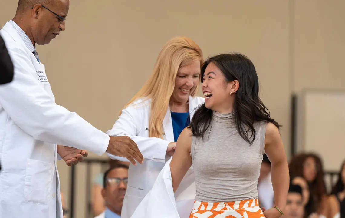 Female medical student receiving assistance putting on her white coat while smiling