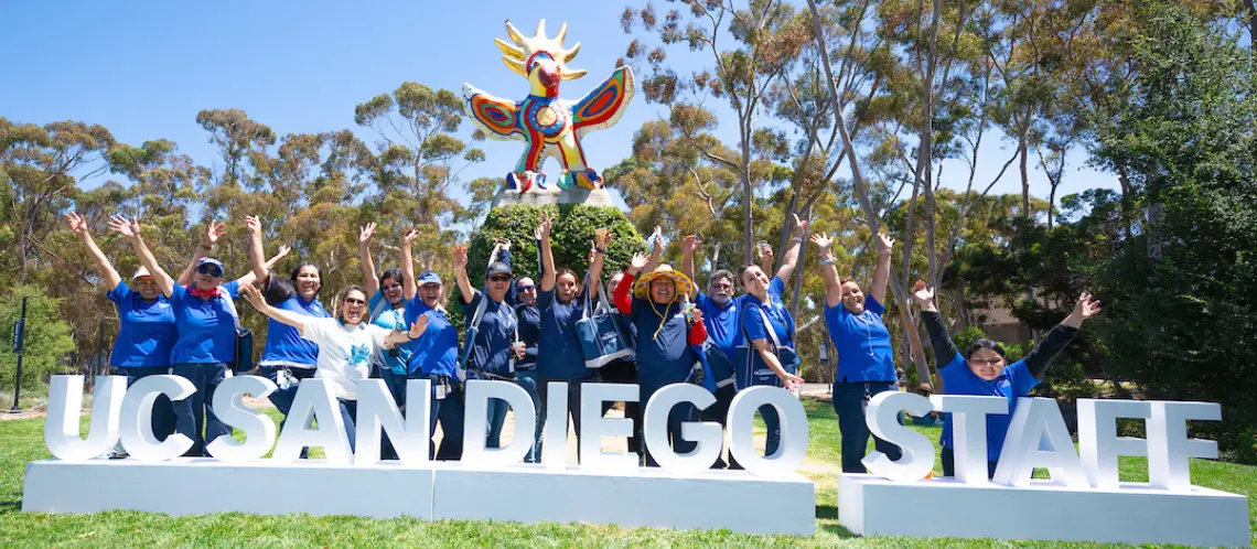 UC San Diego staff members pose for a group photo next to large letters that spell out 