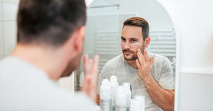 Person looking in mirror applies white cream to face