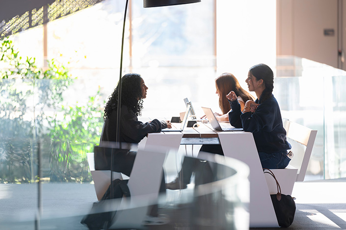 Three students sit at table on laptops
