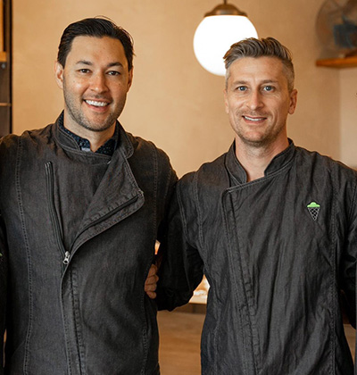 Two men in ice cream aprons pose and smile for a picture. 