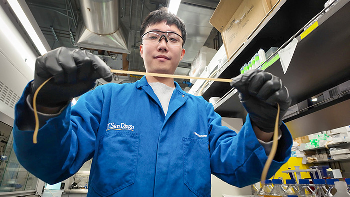 Man in blue lab coat hold a stretchy strip of material.