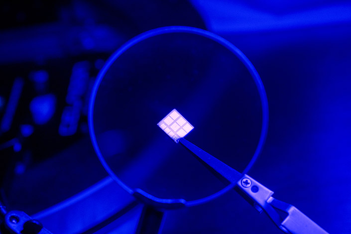 A small chip held by tweezers under a magnifying lens.