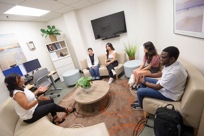 Five people sit on curved sofas in a circle with a short table in the middle of the group.