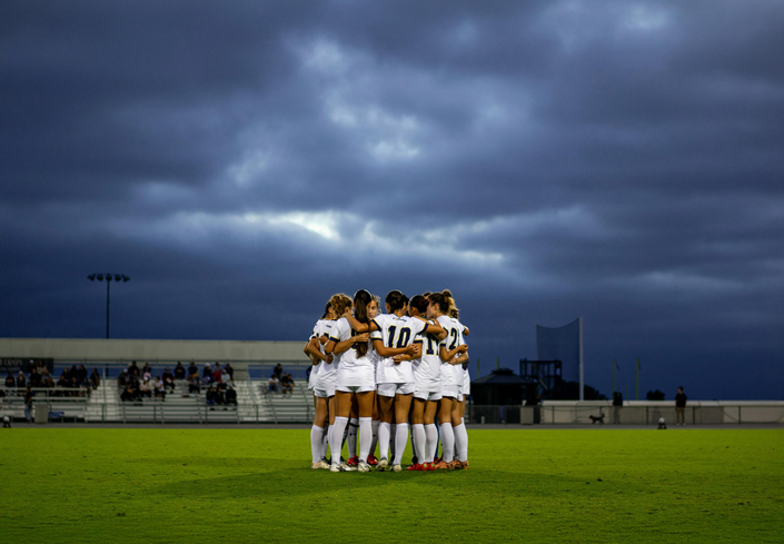 A women’s soccer team in their pre-game huddle stands under an ominous night sky. (Photo by Arwyn Guinto)