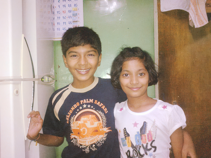 Two children smile standing in a kitchen.