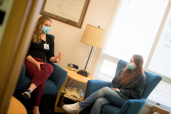 A female therapist speaking with a female student in a comfortable space about mental health.