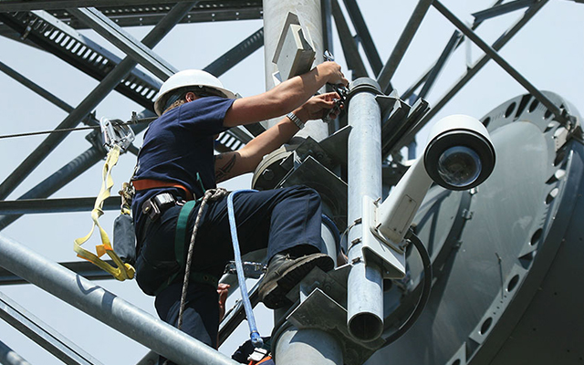 An engineer installs an antenna on a microwave tower to connect a nearby fire station to HPWREN.