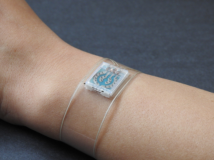 Clear band with small electronics worn on a person's wrist.