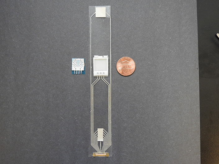 Clear strip with small electronics attached to it, next to a penny.