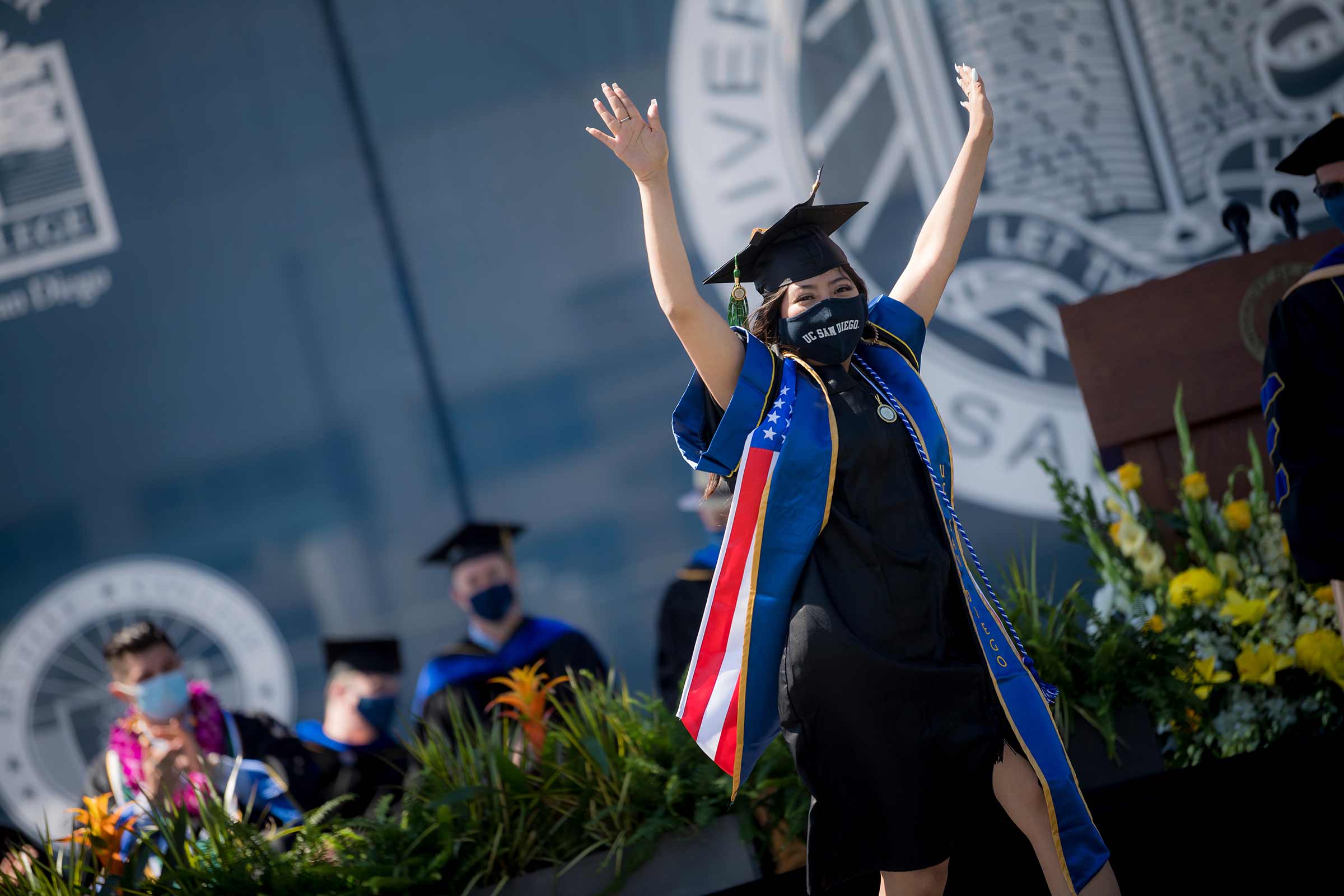 UC San Diego student raises her arms in celebration as she crosses the stage.
