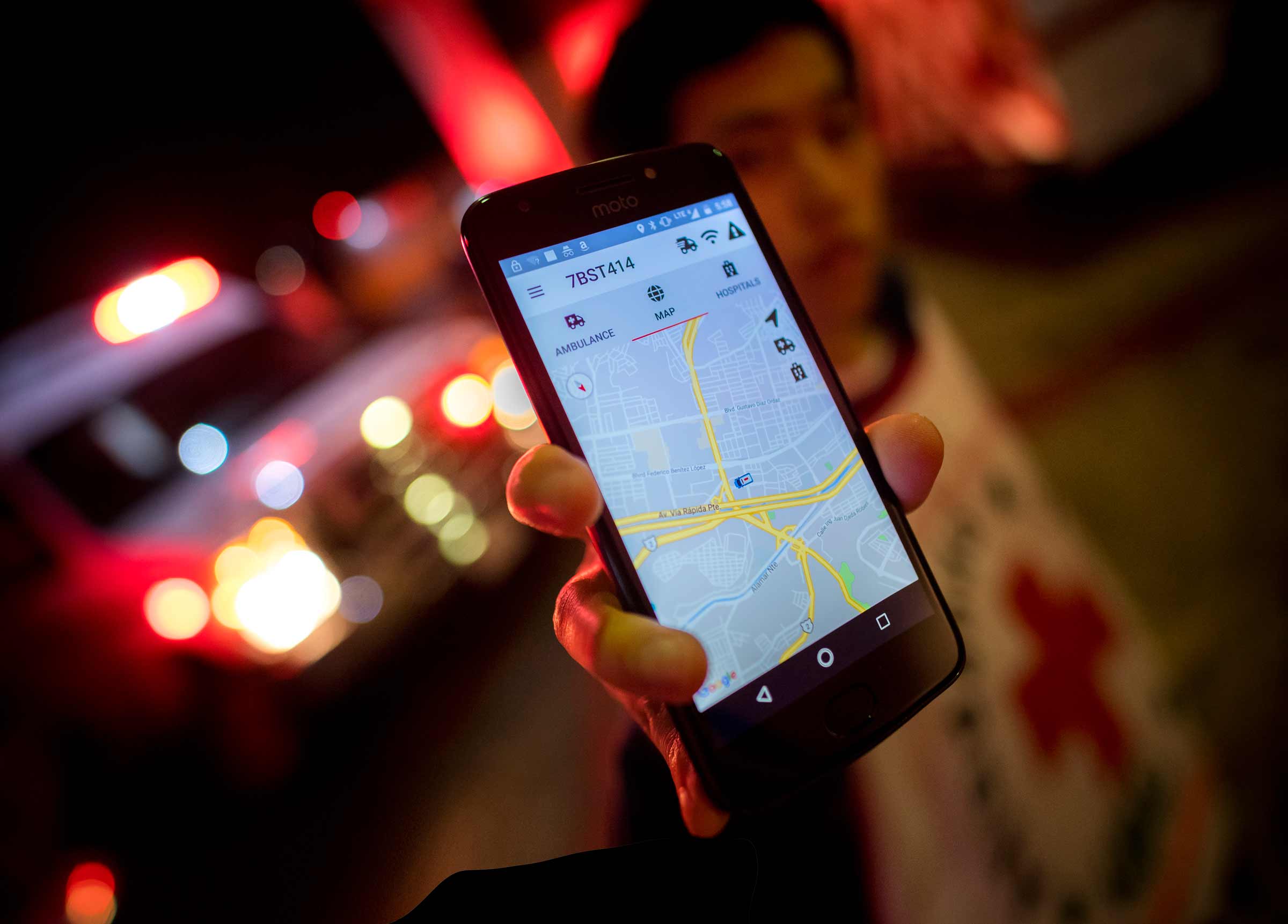 A student holds out their phone to show the app with red ambulance lights in the background