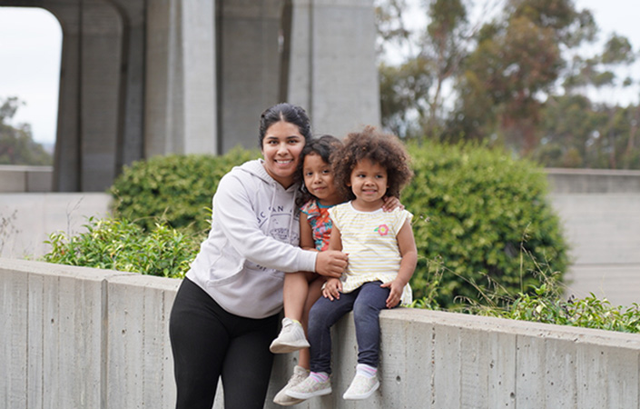 A student parent with her two daughters sitting outside of Geisel Library at UC San Diego.